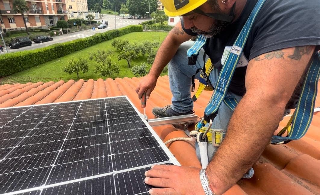 Un installatore avvita la staffa di un pannello fotovoltaico su un tetto in coppi